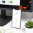 A smartphone displays analytics data with graphs showing views, downloads, and likes. It is resting vertically on a white dock next to a small potted succulent plant. In the background, a large computer monitor is partially visible, along with a closed laptop and a white wireless earbud case.
